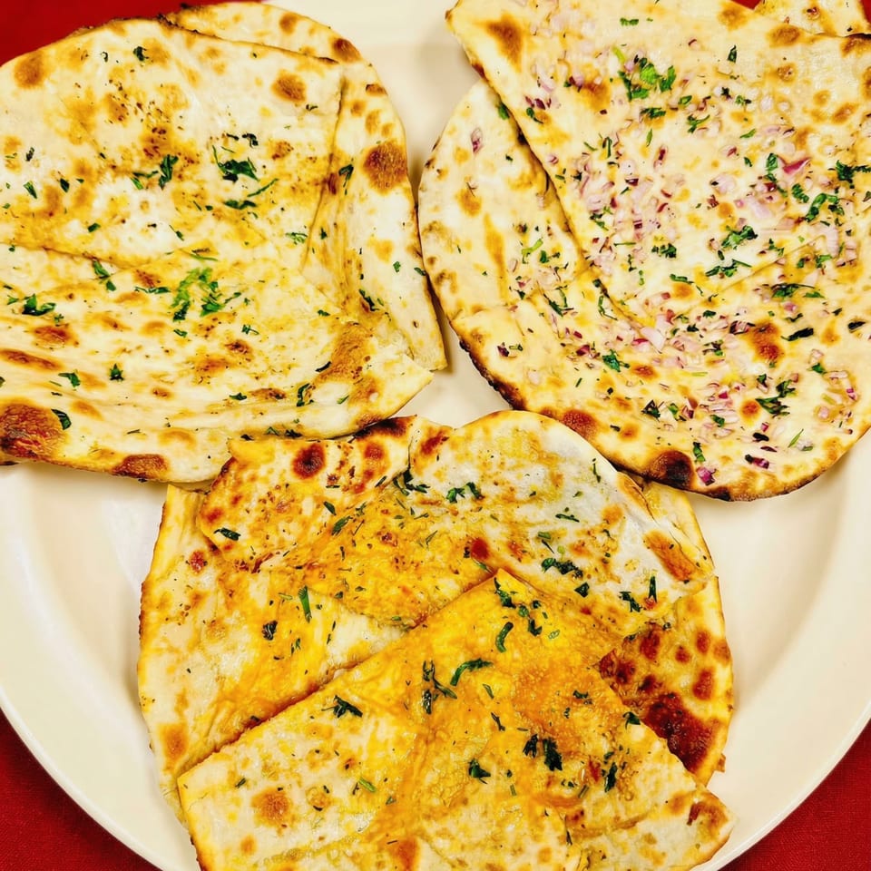 Three different Indian naan breads, including garlic and onion, on a white plate.