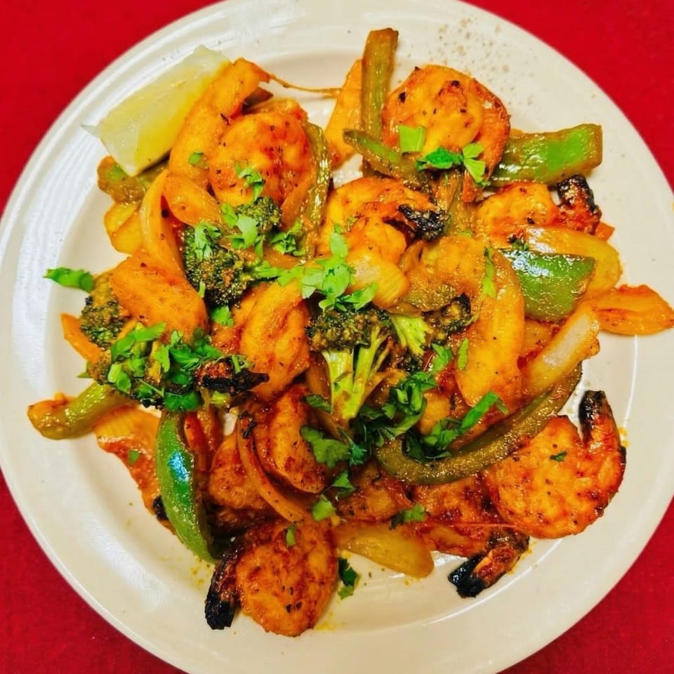 Indian shrimp dish with broccoli, bell peppers, onions, and cilantro, served with a lemon wedge.