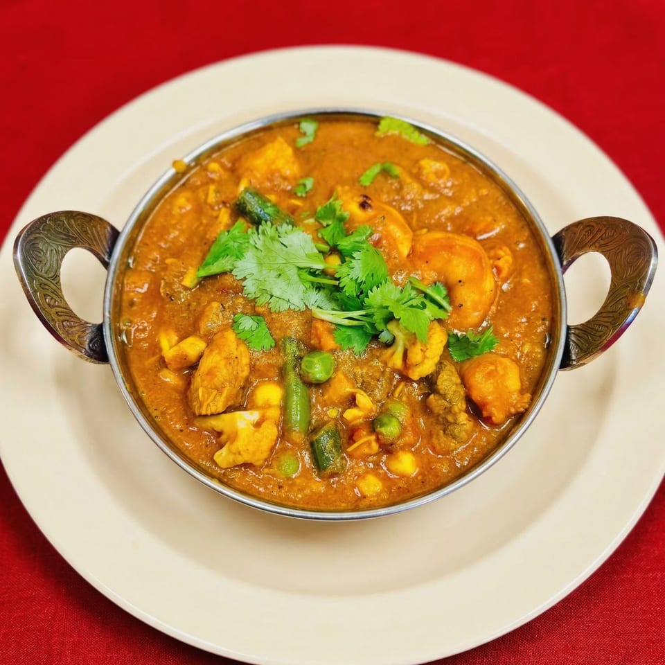 Indian curry with chicken, vegetables, and cilantro in a metal bowl on a white plate.