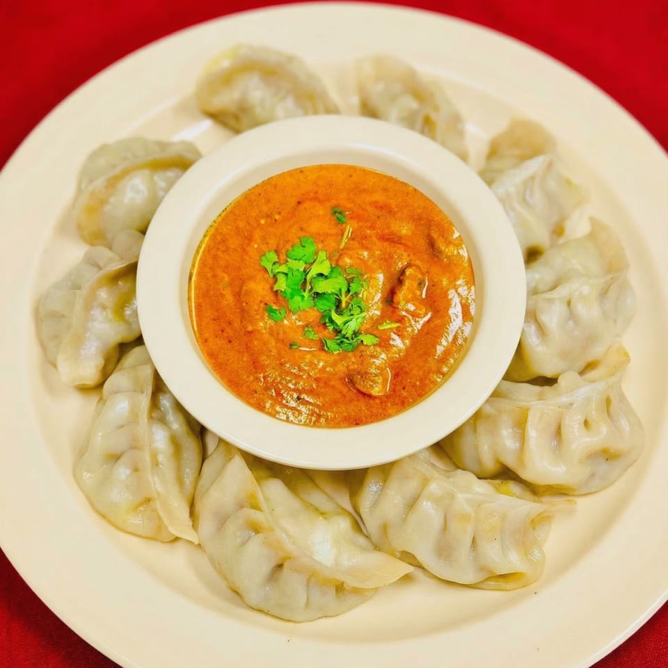 A plate of steamed momos surrounds a bowl of orange curry sauce garnished with cilantro.