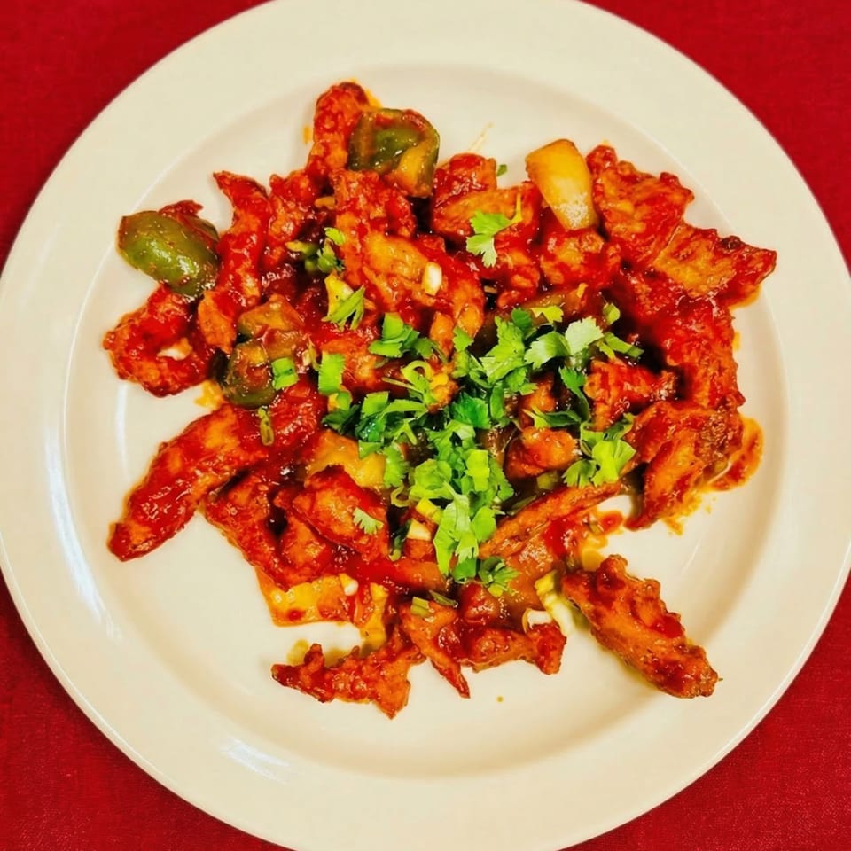 Chili chicken with green peppers and cilantro on a white plate from Masala & Curry.