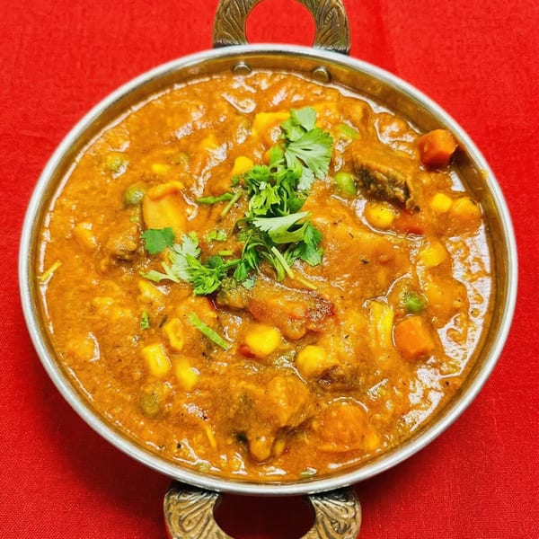A close-up of a vibrant Indian curry with vegetables and meat, garnished with fresh cilantro, in a metal bowl.
