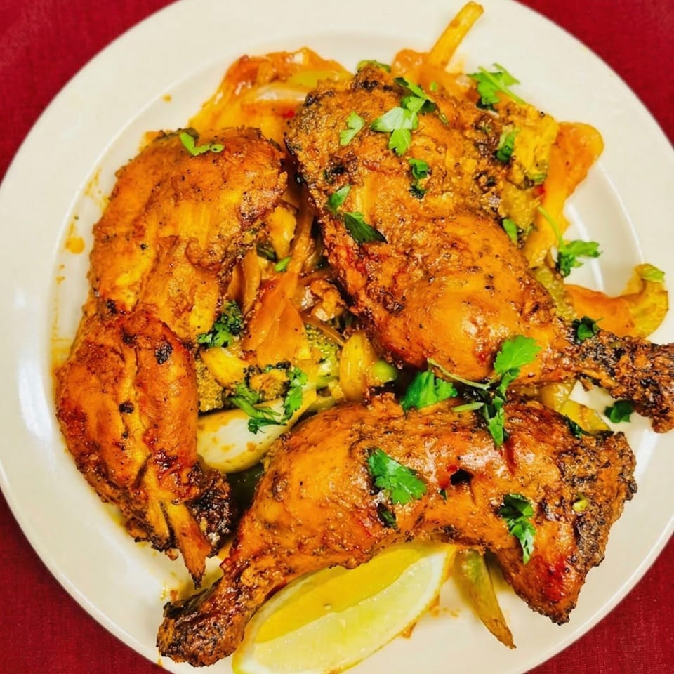 Three pieces of Indian tandoori chicken, garnished with cilantro and a lemon wedge, on a white plate.